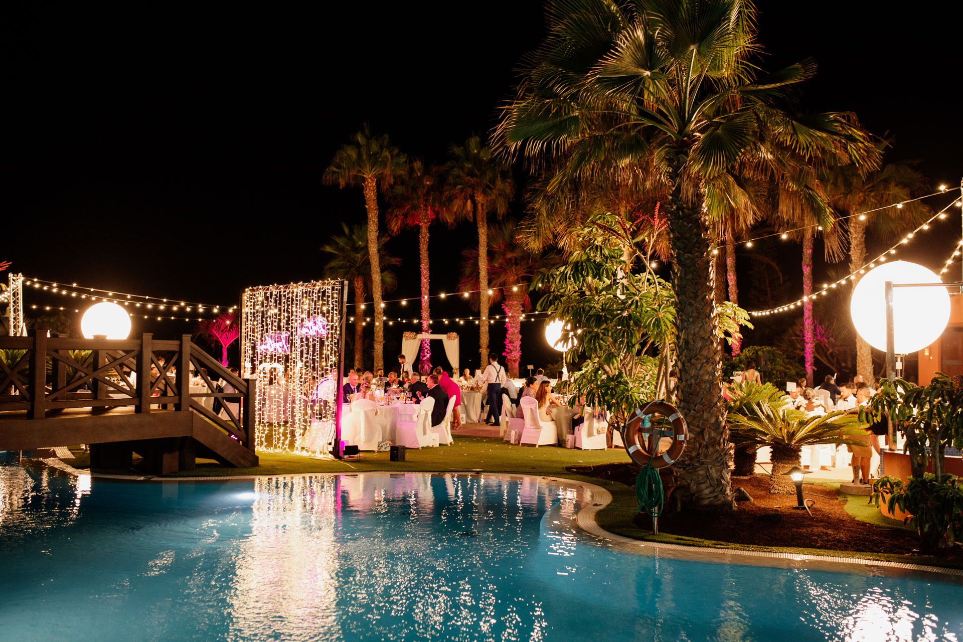 Cena exterior de la boda de Alexandra e Iñaki en el Hotel Sheraton La Caleta, con decoración de mobiliario e iluminación cálida en los jardines.