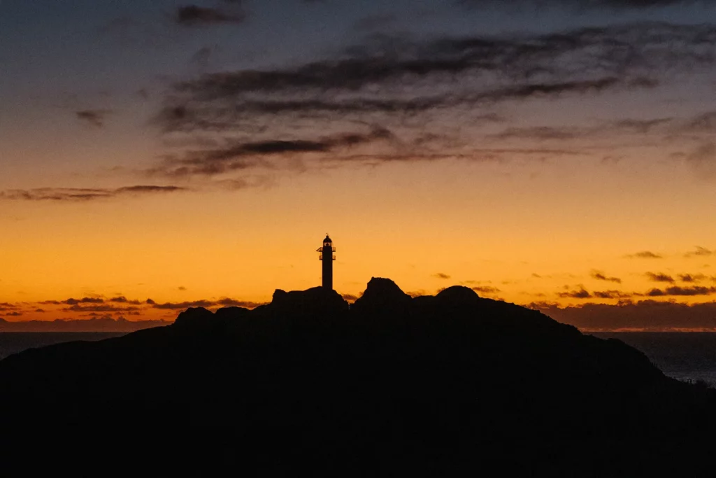 Marina y Rubén en su boda en el paraje natural de Punta de Teno, con el faro y los acantilados de fondo al atardecer.